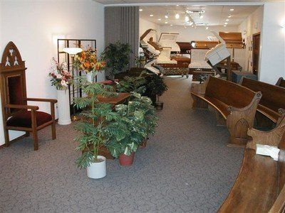 Quiet indoor waiting area with wooden benches, potted plants, and furniture in a bright showroom-like room