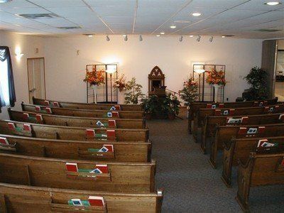 Empty chapel with wooden pews facing a central altar and floral arrangements.