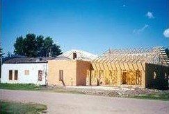 Two small houses with a blue sky, one white and one yellow under construction on a roadside.