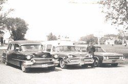 Three vintage classic cars parked side by side on a sunny street.