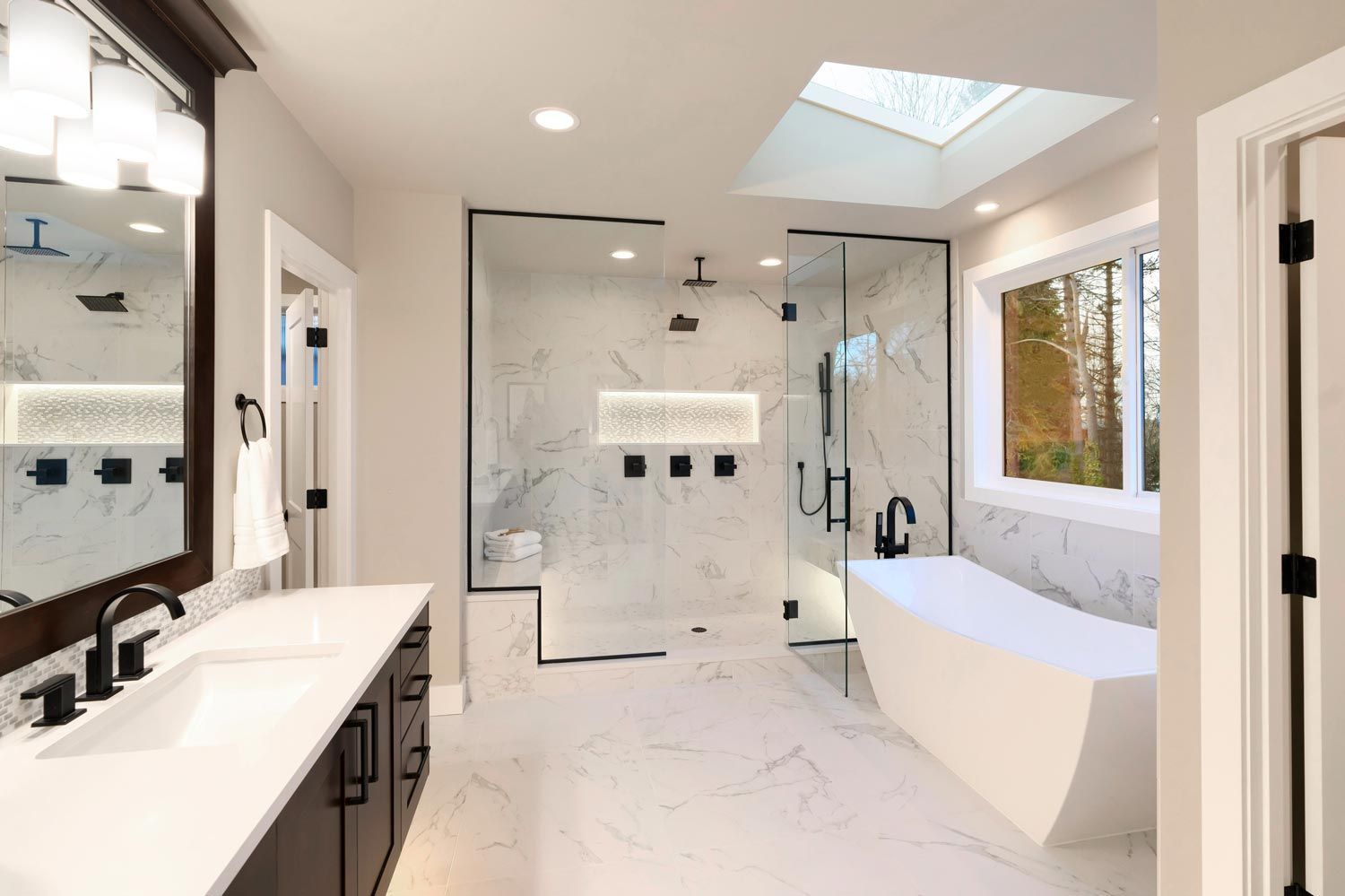 Bright modern bathroom with double vanity, glass shower, freestanding tub, and large window Bright modern bathroom with double vanity, glass shower, freestanding tub, and large window