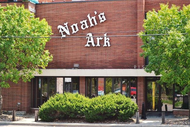 Brick building with “Noah’s Ark” sign above entrance, framed by green trees and shrubs.