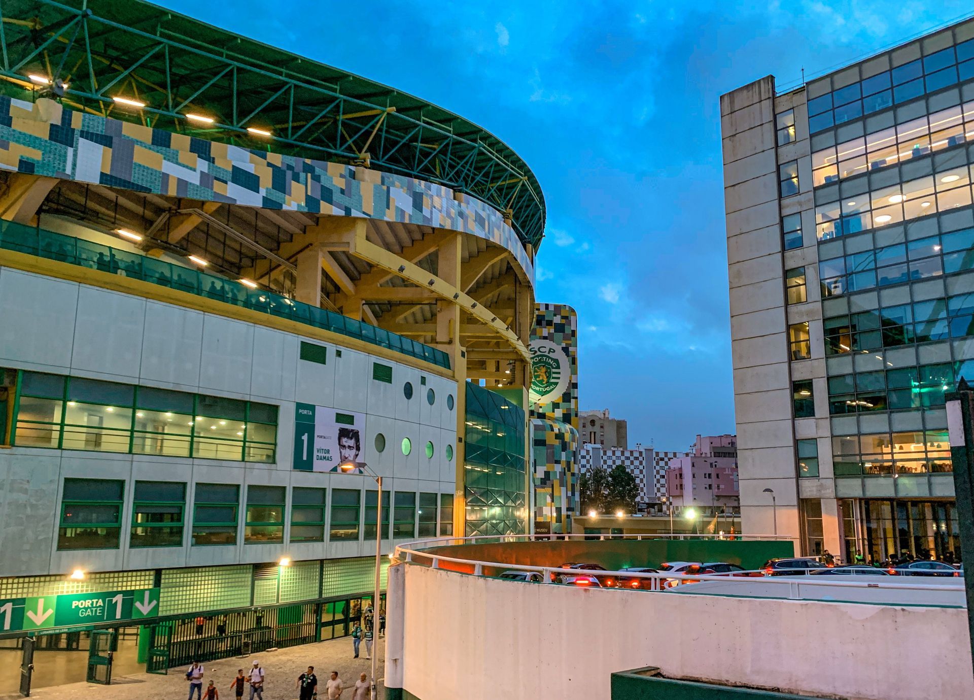 Modern stadium and office buildings at dusk under a blue sky in an urban setting
