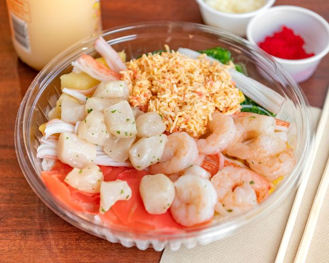Seafood rice bowl with shrimp, scallops, crab, and garnishes in a clear plastic container