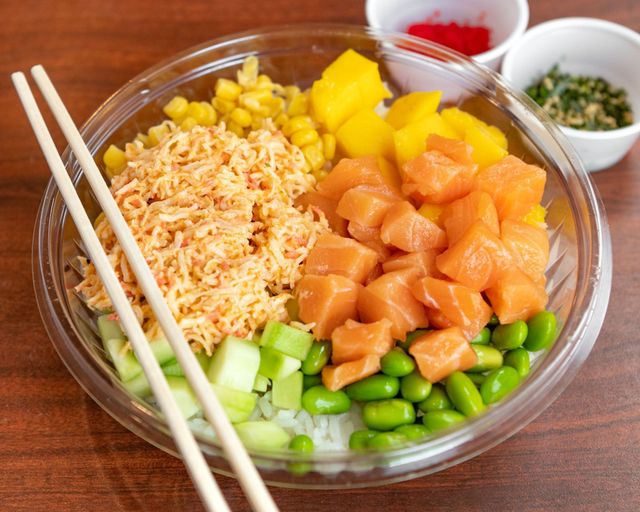 Poke bowl with salmon, rice, edamame, cucumber, mango, and corn, with chopsticks on the side