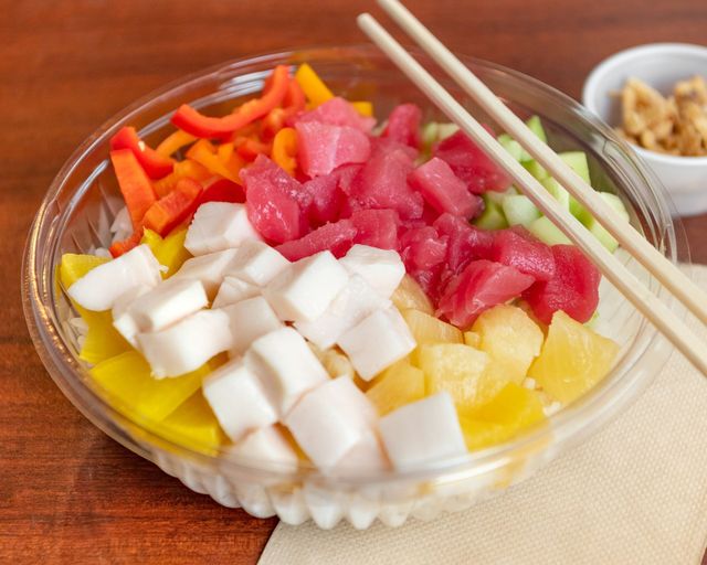 Colorful poké bowl with diced fish, fruit, vegetables, and chopsticks on a wooden table