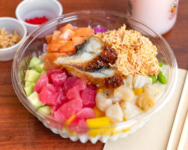 Colorful poke bowl with diced tuna, avocado, mango, cucumber, and rice on a wooden table