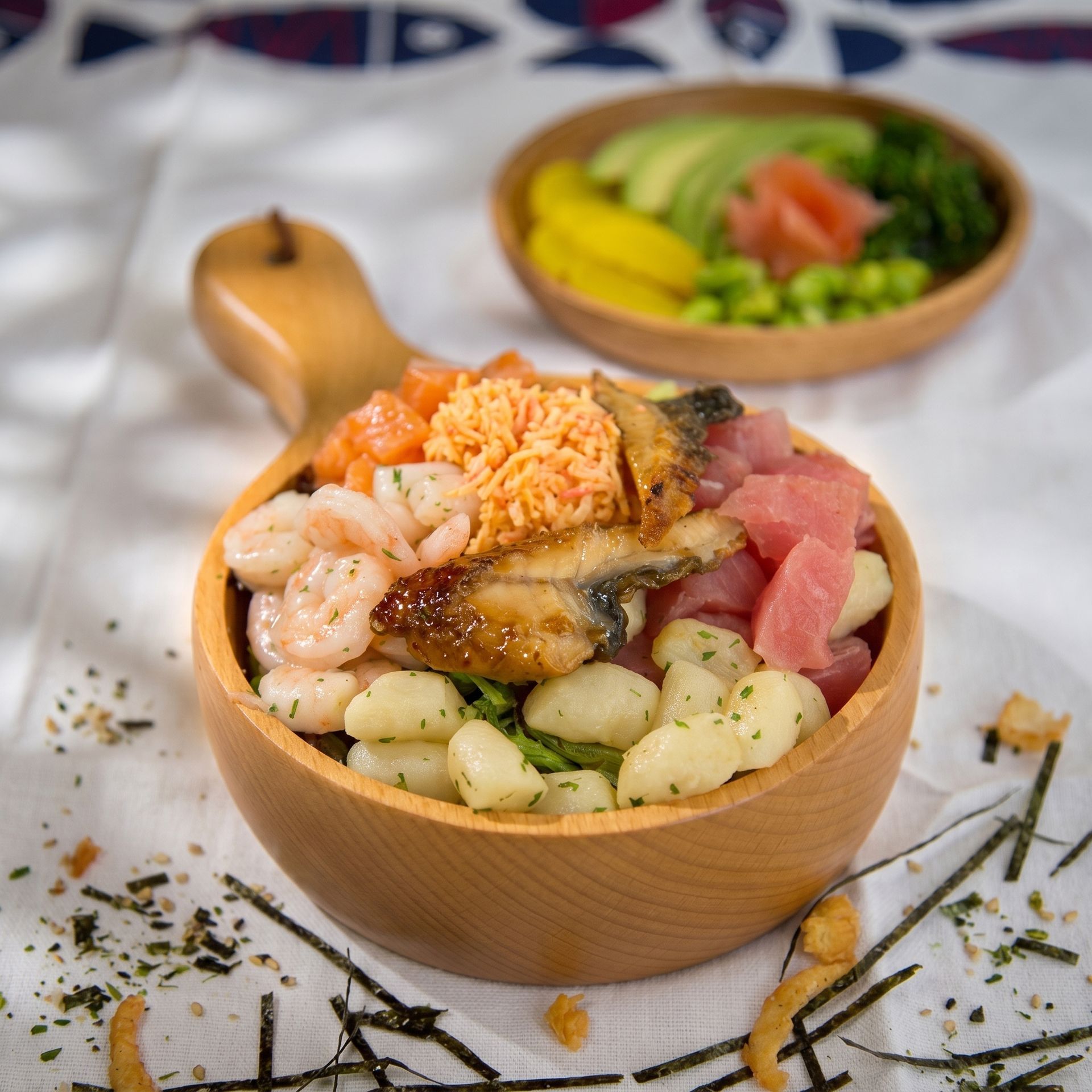 Wooden bowl of mixed seafood and vegetables on a white table, with a second bowl in the background