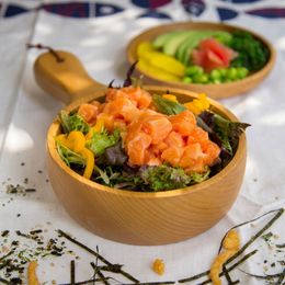 Wooden bowls of salmon salad with greens and avocado on a white tablecloth