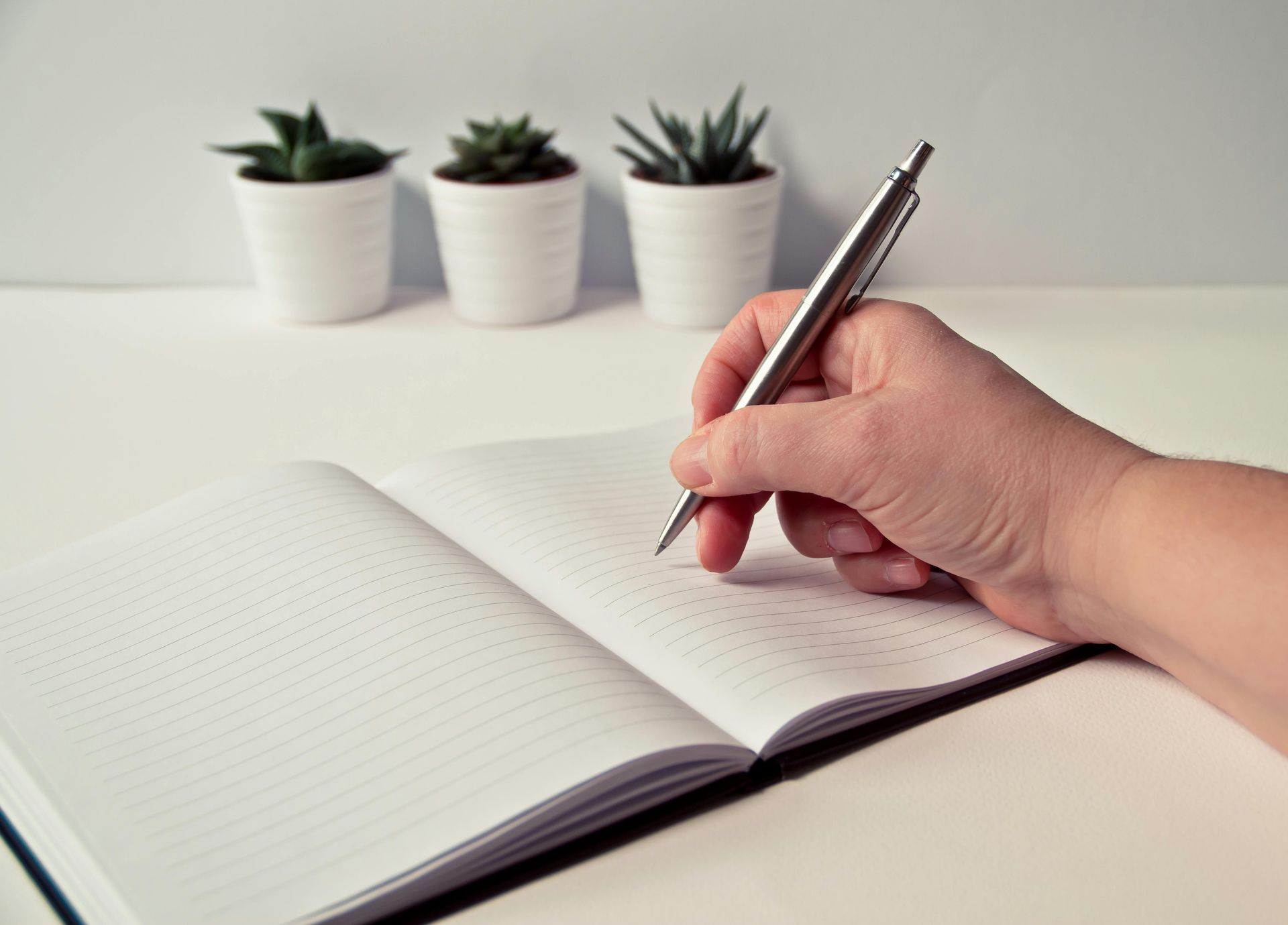 Person writing in a notepad with greenery in the background, symbolizing mindful planning.