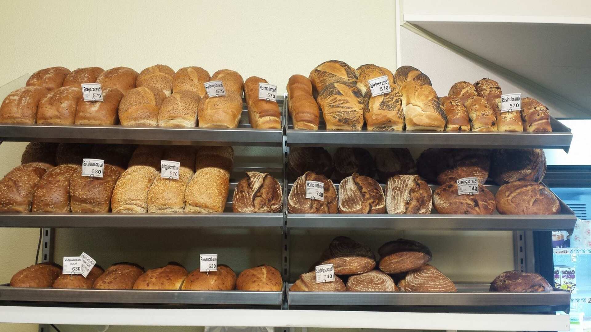 A variety of breads are displayed on shelves in a bakery.