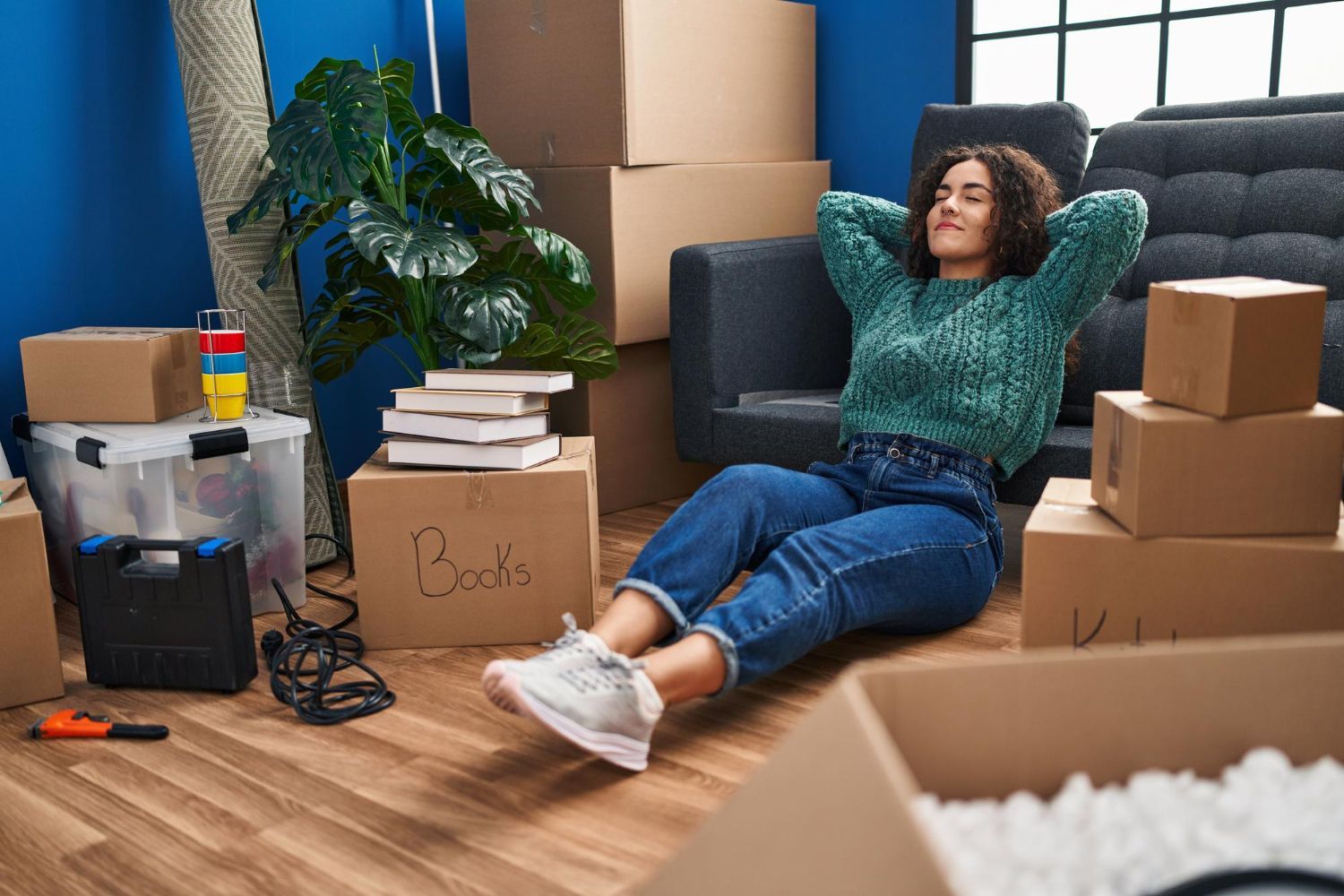Woman relaxing on the floor among moving boxes and packed books in a living room