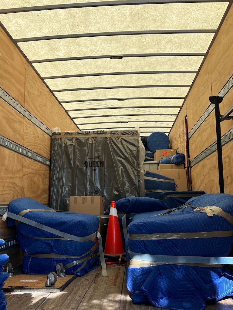 Truck interior packed with blue-wrapped furniture, a red cone, and an orange tarp covering cargo at the front.