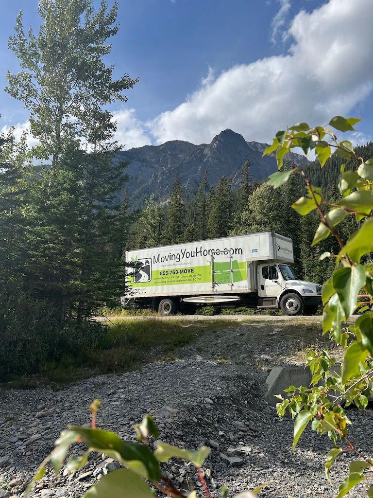 A moving truck is parked on a gravel road in front of a mountain.