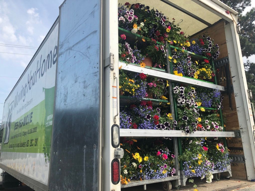 A truck filled with lots of flowers is parked on the side of the road.