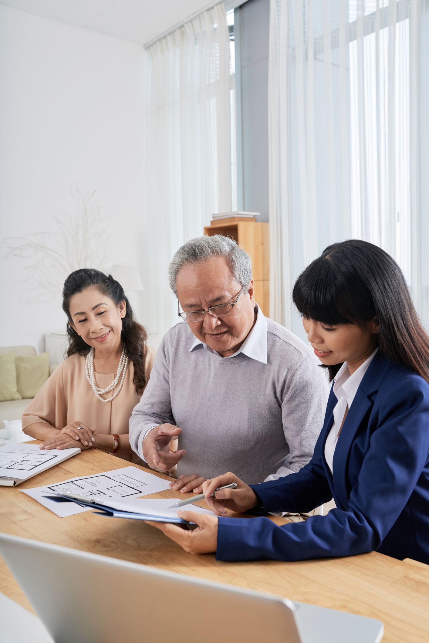 Three people review documents at a table in a bright office, discussing papers and charts.