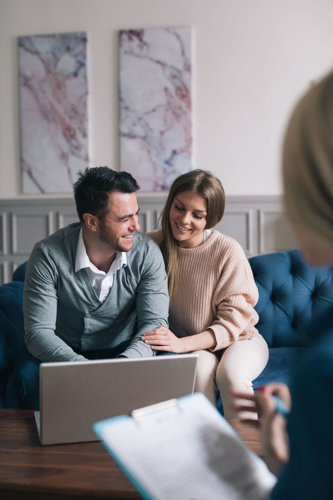Couple smiling on a couch using a laptop during a home meeting