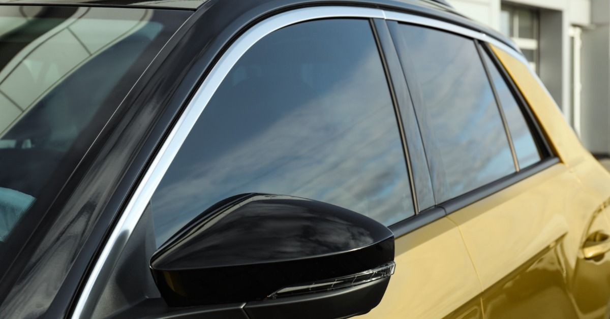A yellow car with tinted side windows, black side mirror, chrome trim, and building reflections on t