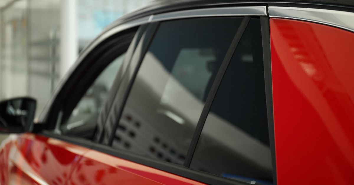 A close-up of a red car side window with dark tinting film, glossy reflections, and an indoor background.