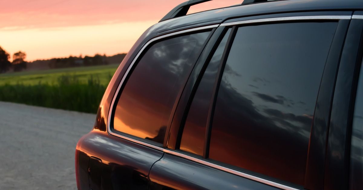 A dark SUV parked on a rocky dirt road, with a red sunset reflecting across tinted rear windows and 