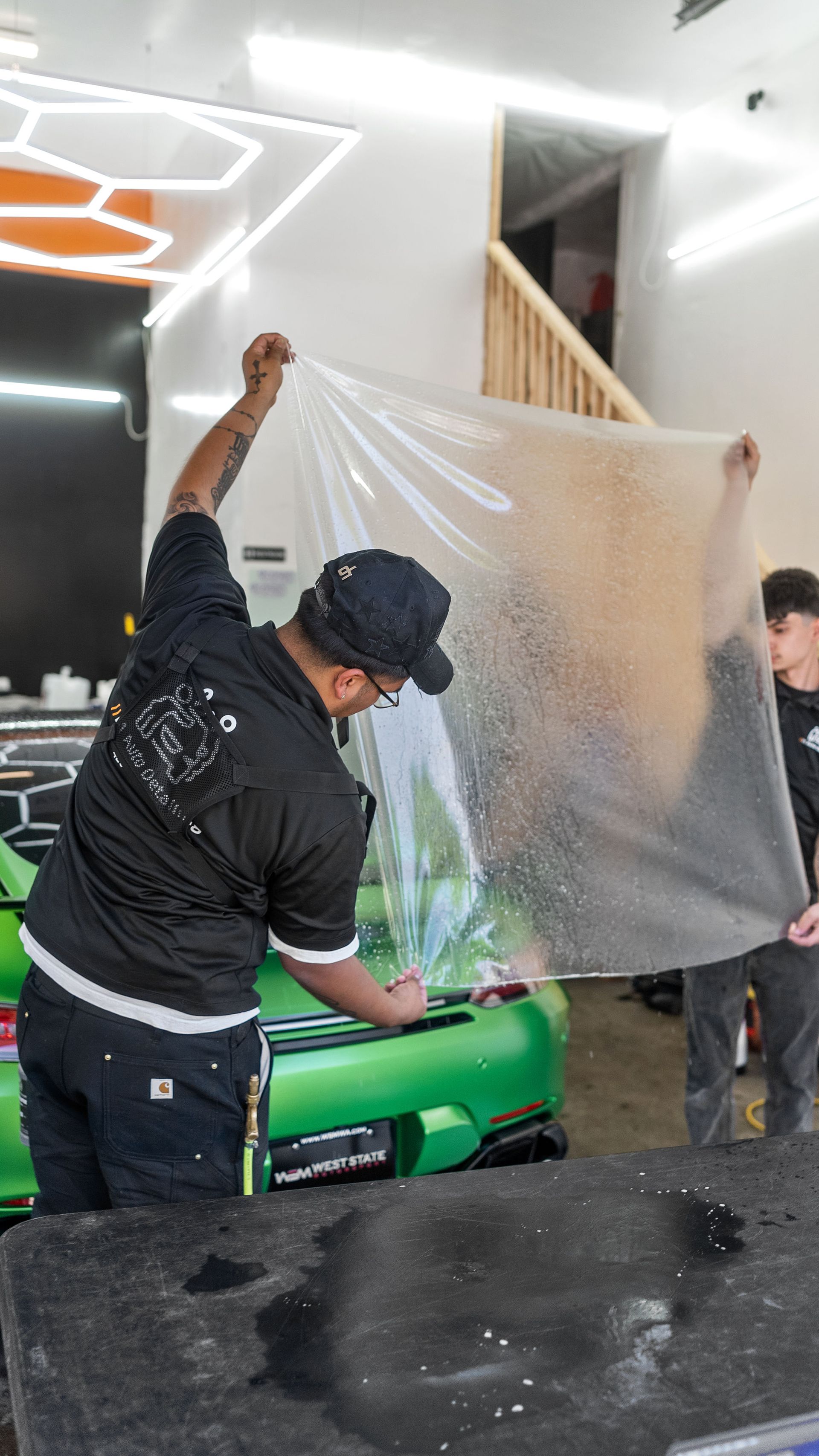 Technician applying vinyl wrap film to a car hood