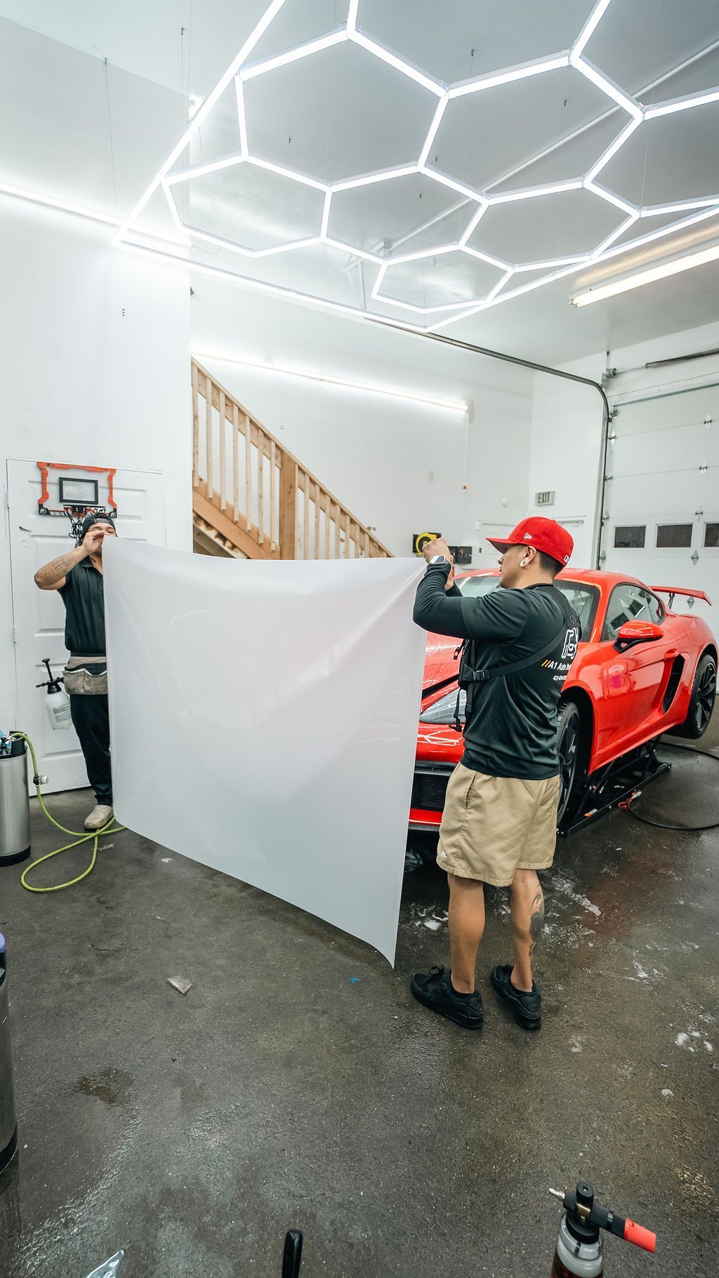 A1 Auto Detailing installers unrolling STEK paint protection film beside a red Porsche in the Lynnwood shop