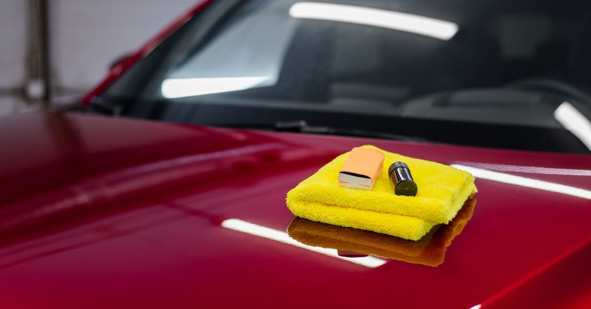 A coating set sitting on a car. The set includes a microfiber towel, sponge applicator, and liquid glass protection.