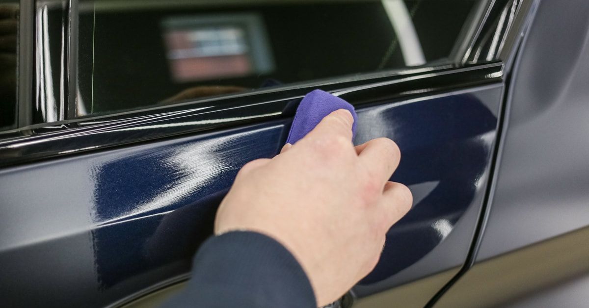 A car service worker running a ceramic coating along the side of a car with a purple bar. The car is blue.