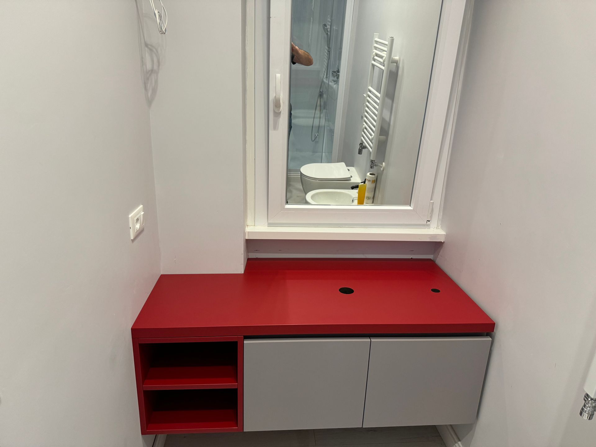 Mobiletto da bagno rosso con lavabo e specchio in un piccolo bagno.