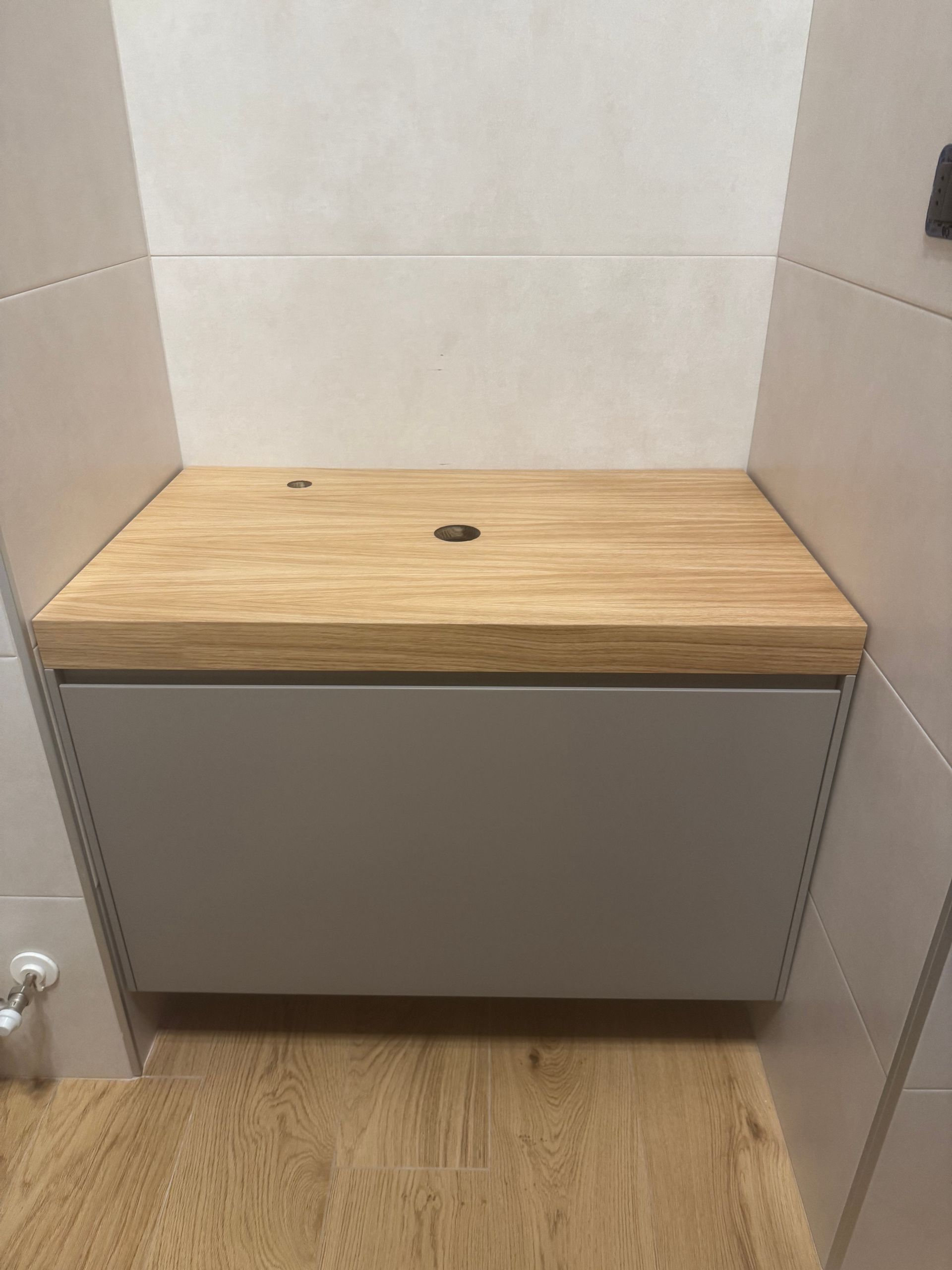 Mobile da bagno con piano in legno e mobiletto grigio in una nicchia piastrellata.