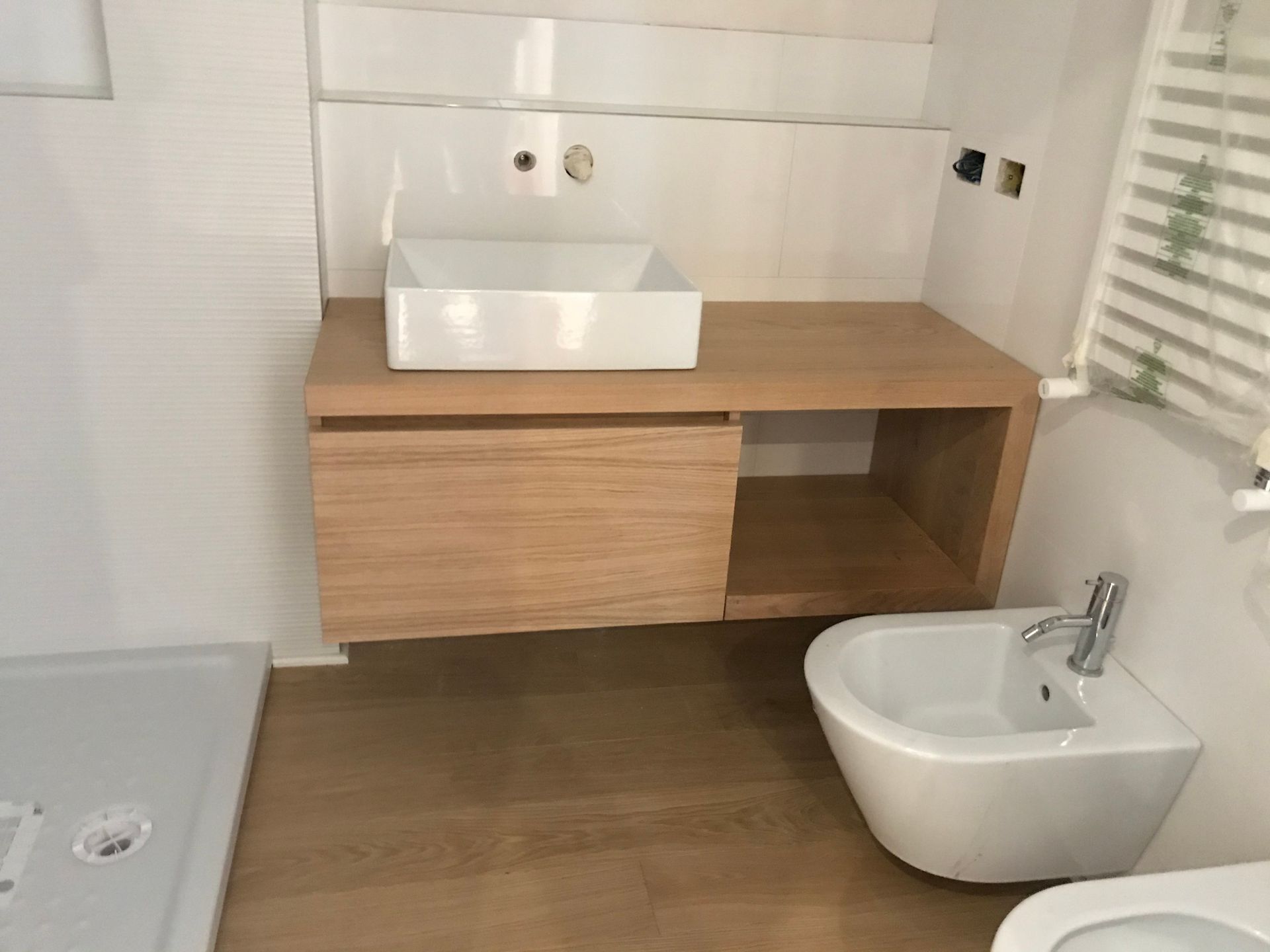 Bagno moderno con mobiletto in legno, lavabo bianco e bidet accanto alla zona doccia piastrellata.