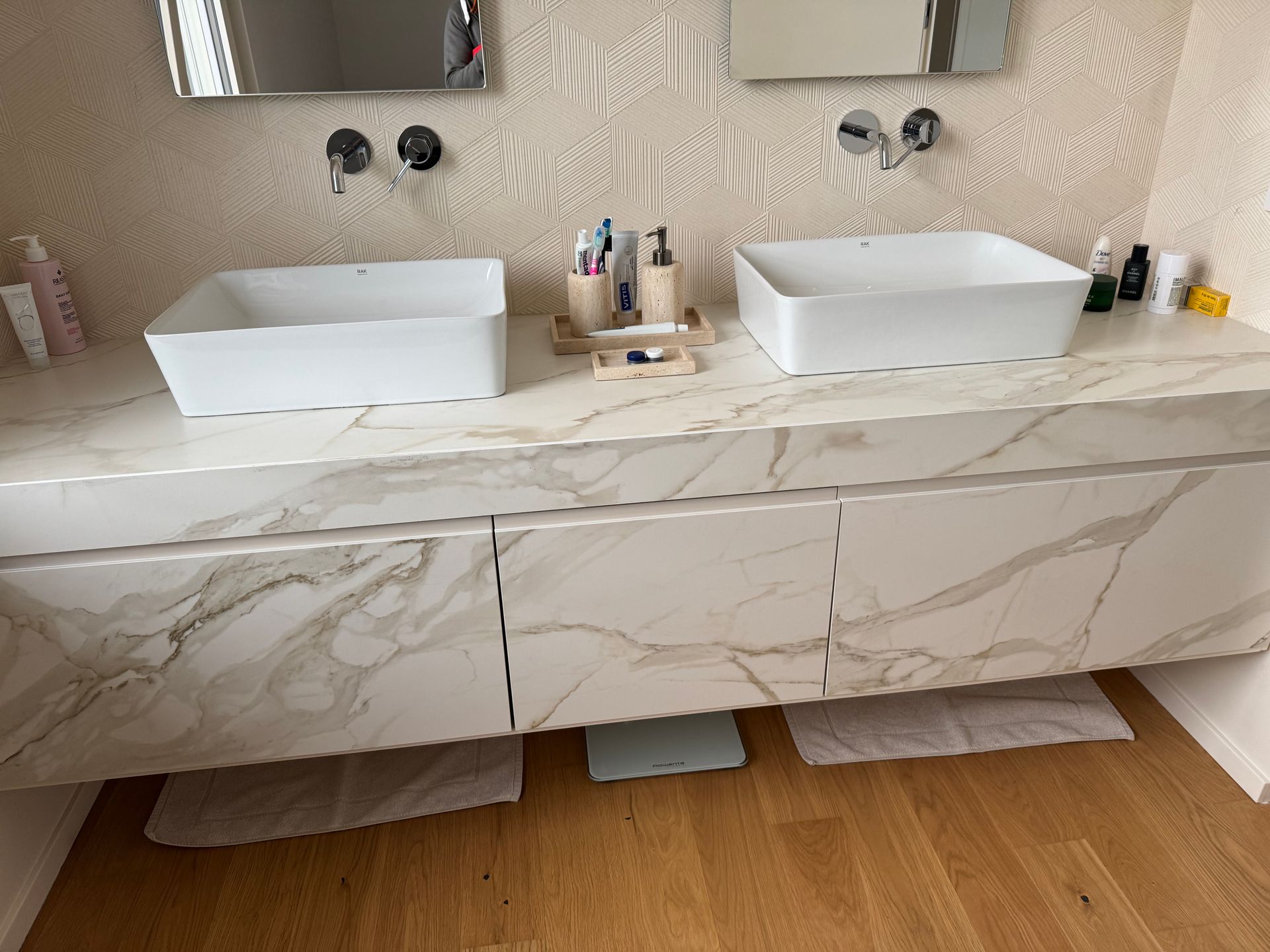 Mobile bagno moderno con due lavabi a ciotola, ante con motivo marmorizzato e pavimento in legno.
