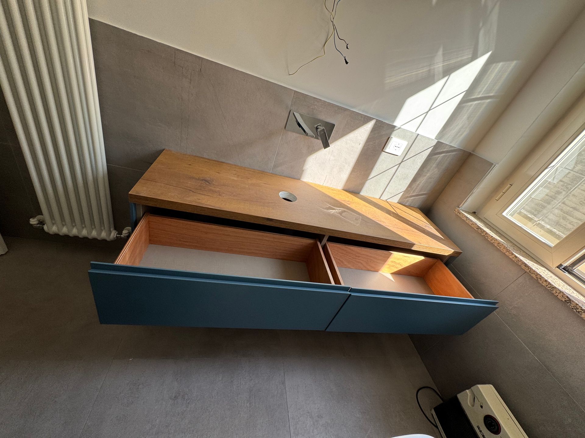 Panca contenitore in legno aperta con pannelli frontali blu in una stanza soleggiata