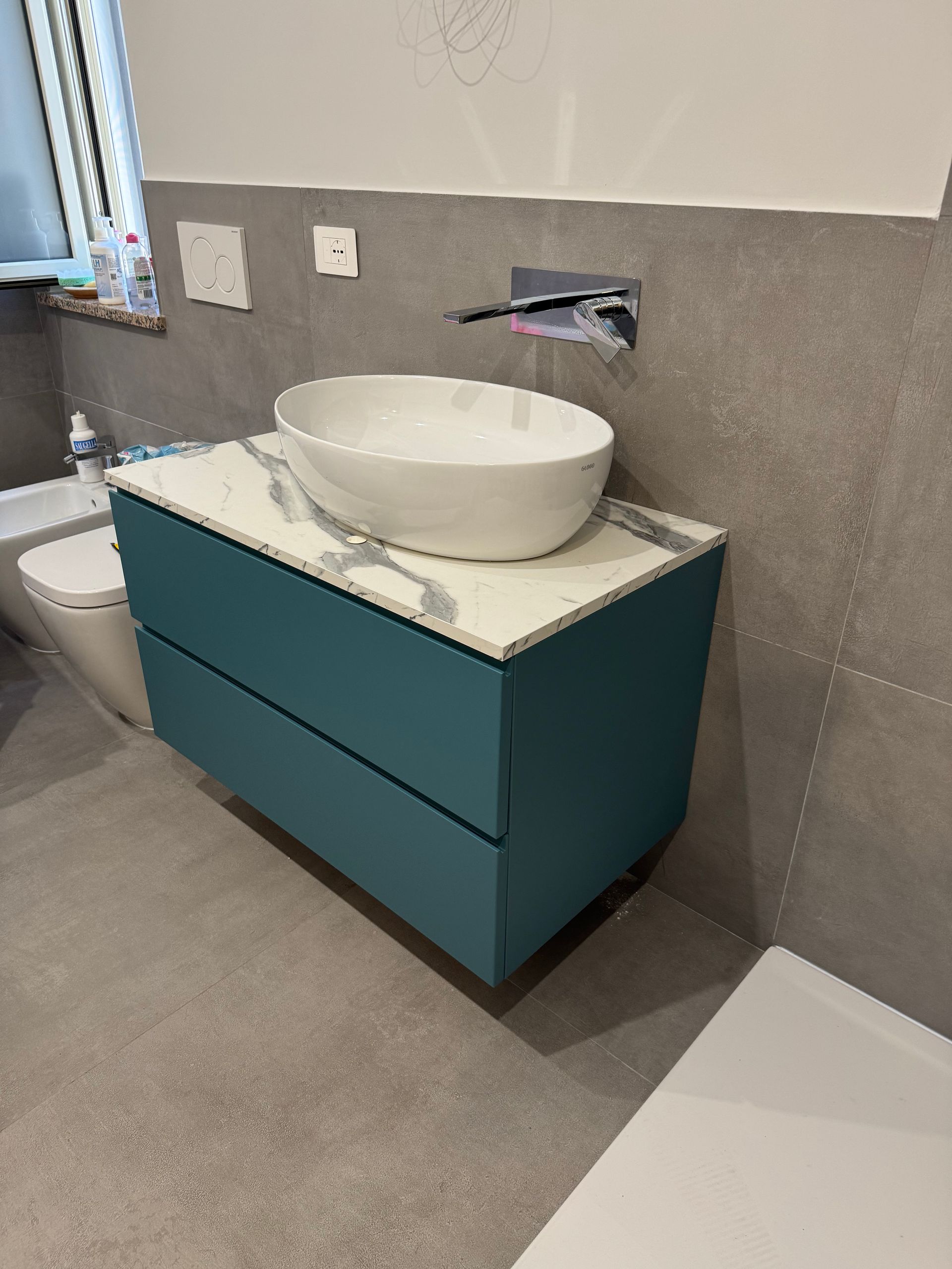 Mobile bagno moderno con cassetti color verde acqua e lavabo a ciotola bianco su una parete grigia.