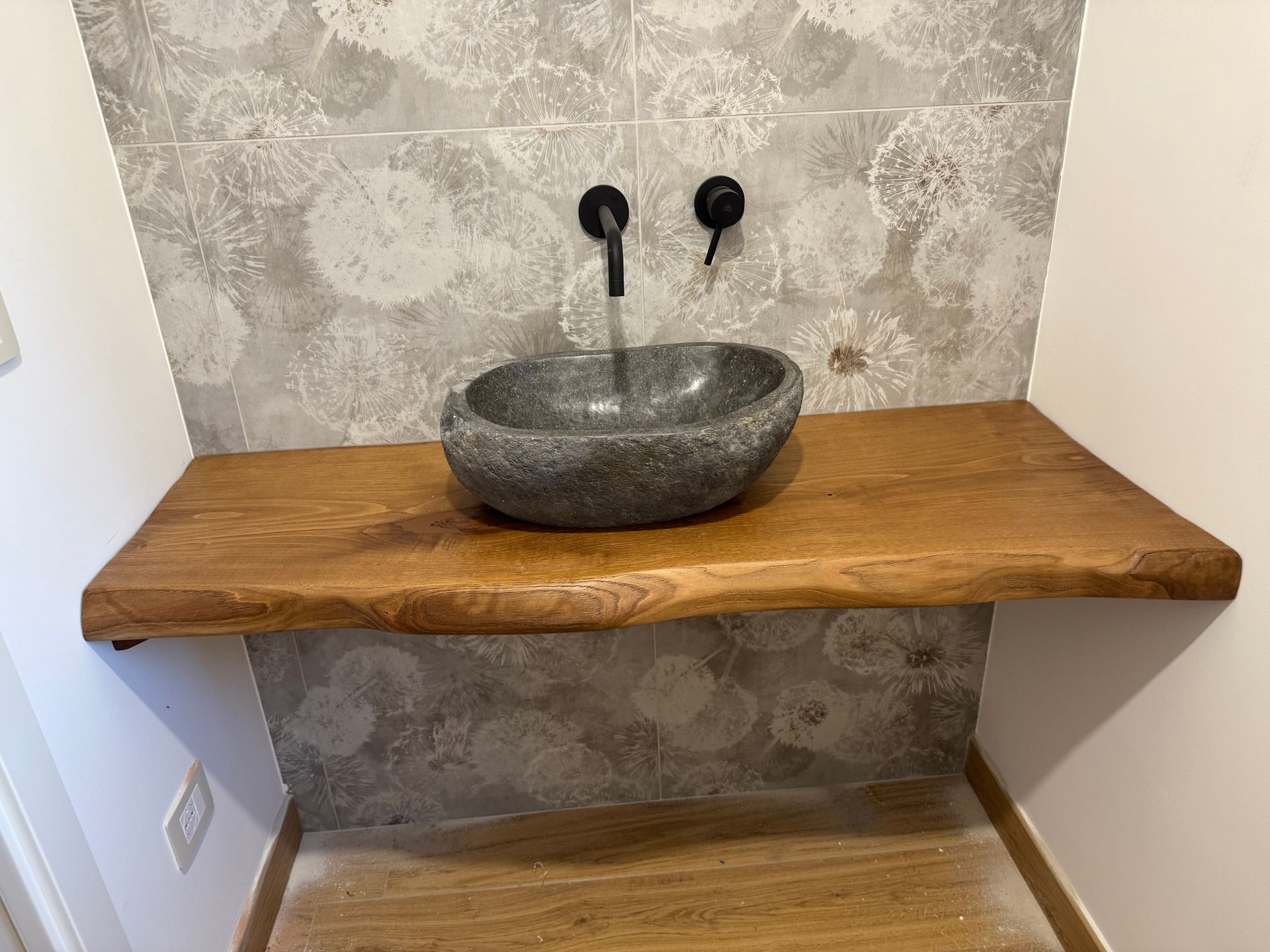 Lavabo rustico in pietra su un robusto piano di lavoro in legno, sullo sfondo di una carta da parati a motivi