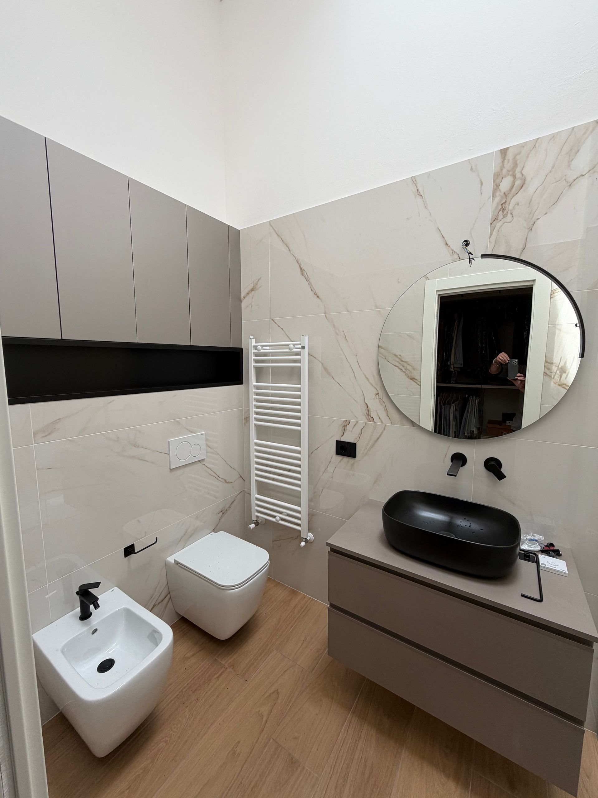 Bagno moderno con WC, bidet, lavabo, grande specchio rotondo e pareti in marmo.