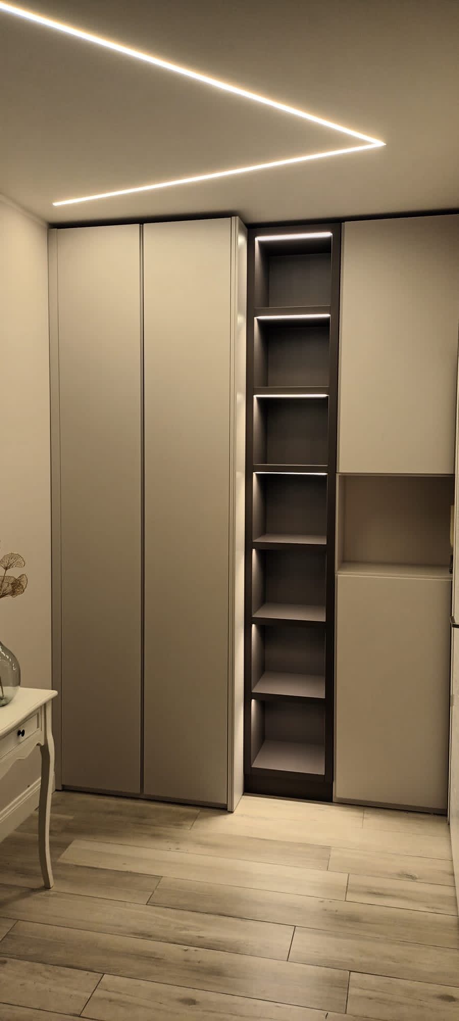 Armadio moderno con ante scorrevoli beige, ripiani a vista e plafoniera a LED diagonale in una camera da letto.