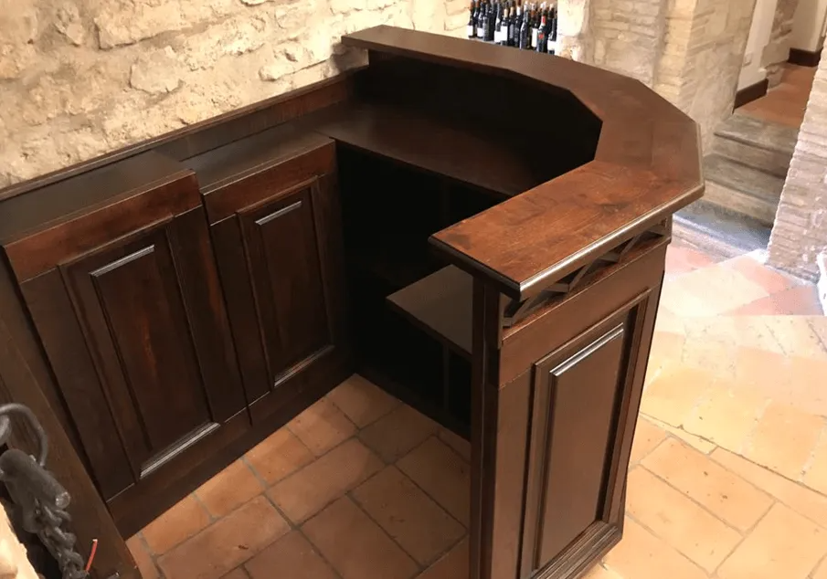Mobile bar angolare in legno scuro con piano d'appoggio in una stanza con pavimento in pietra.