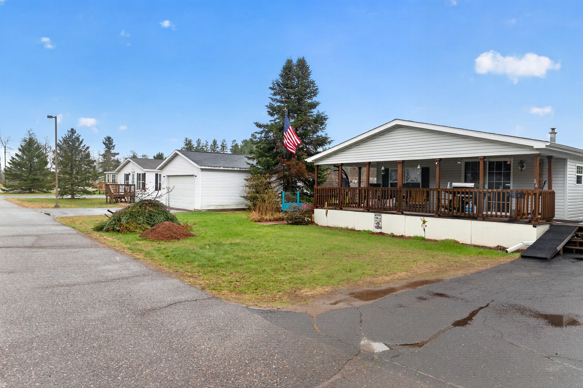 Single-story mobile home with a porch on a grassy corner lot under a blue sky