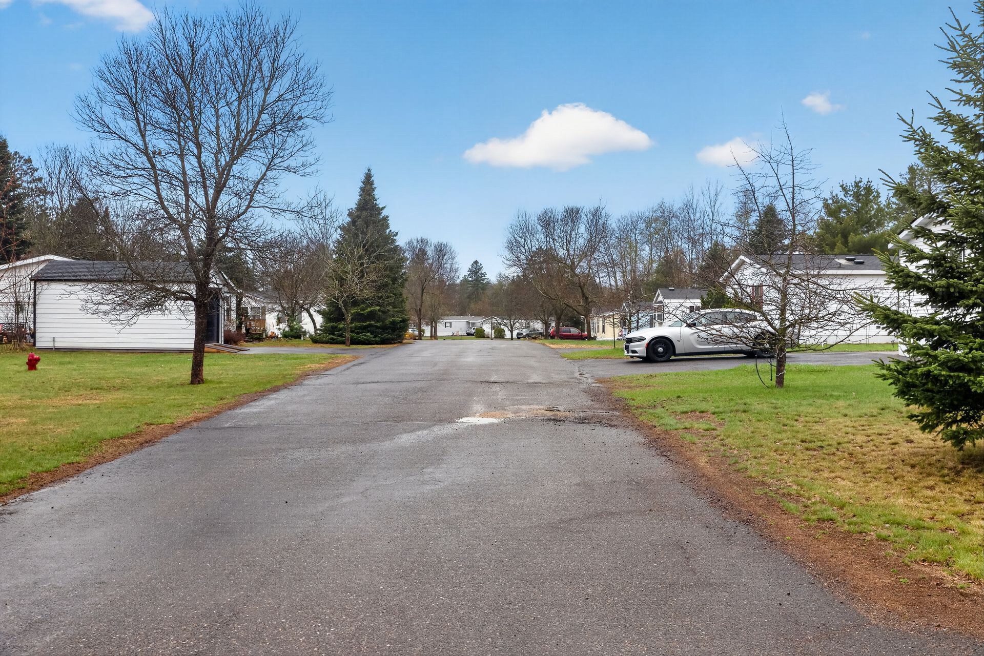 Wet driveway in a suburban neighborhood with white houses, trees, and a parked white SUV under a blue sky