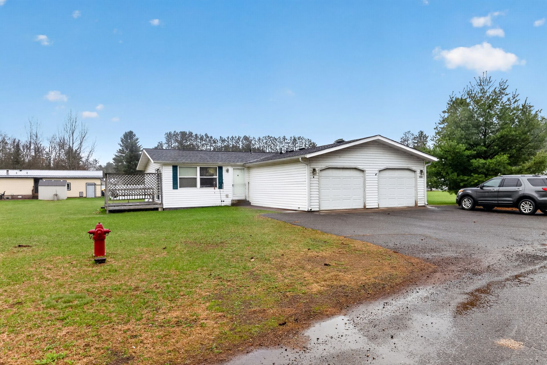 Single-story white house with attached garage, gravel driveway, lawn, and red fire hydrant under cloudy sky