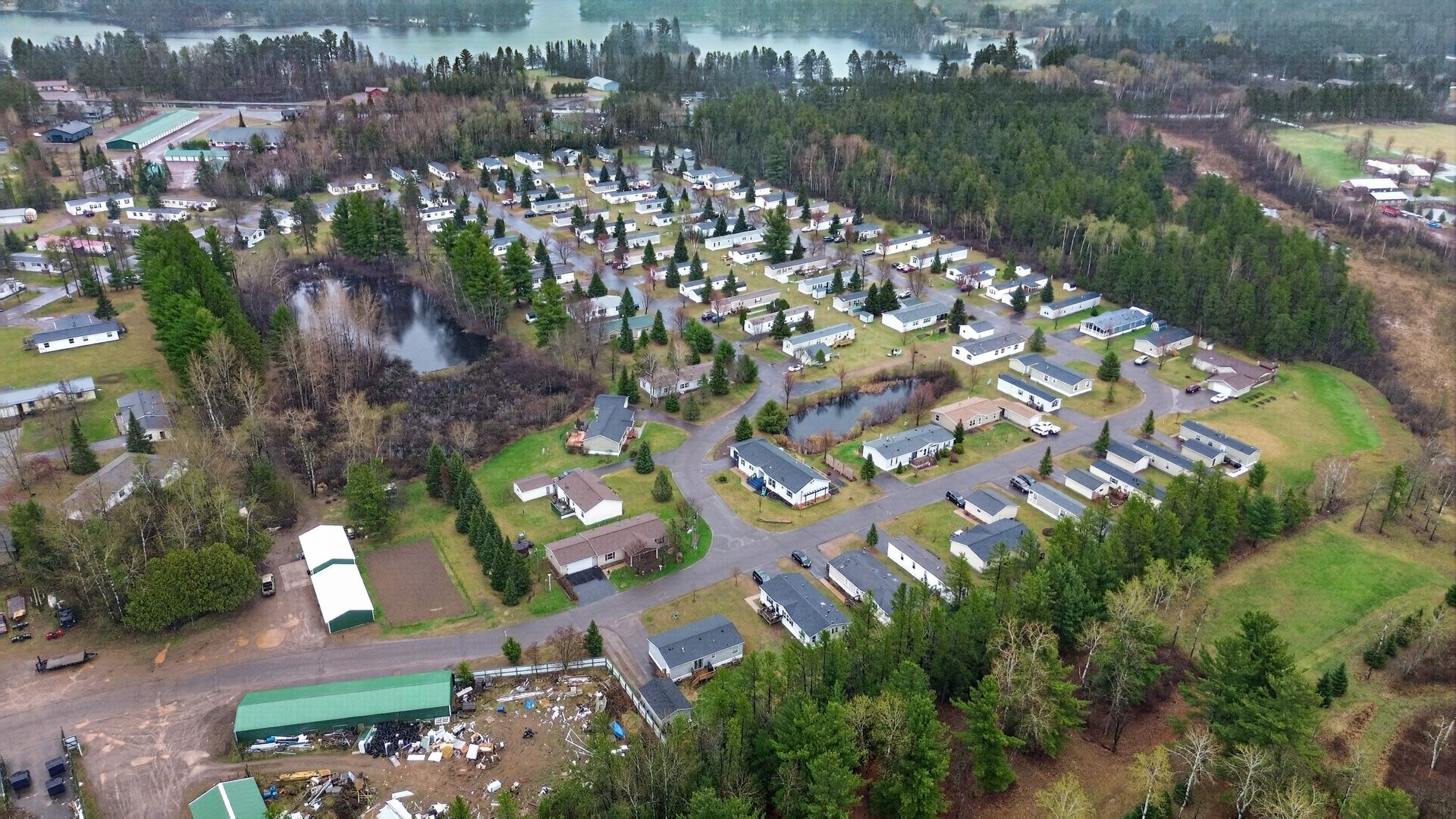 Aerial view of a suburban neighborhood with rows of houses, trees, and a lake in the background.