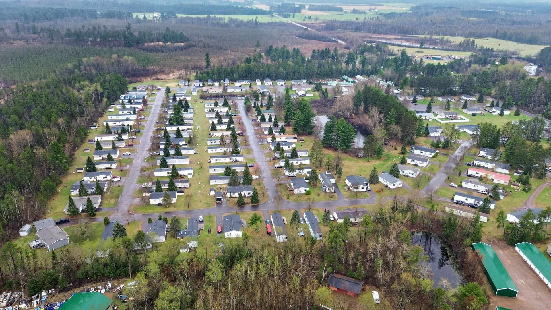 Aerial view of a suburban neighborhood with rows of houses, streets, trees, and open fields in the distance