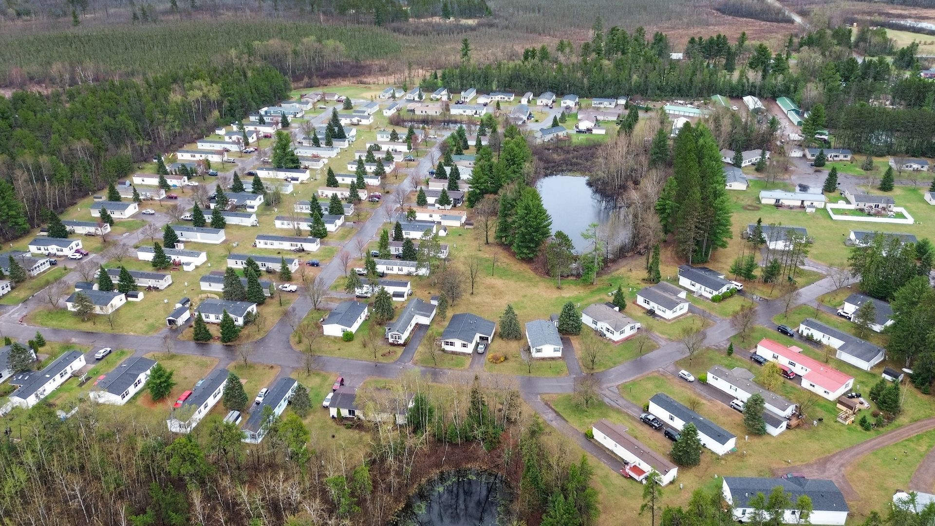 Aerial view of a mobile home park with rows of white trailers around a central pond and trees
