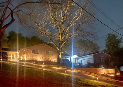 A house is lit up at night with a tree in the foreground.
