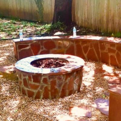 A fire pit is surrounded by a stone wall and gravel in a backyard.