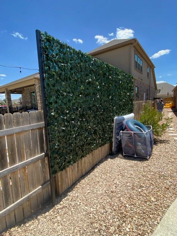 A wooden fence with a green hedge behind it.