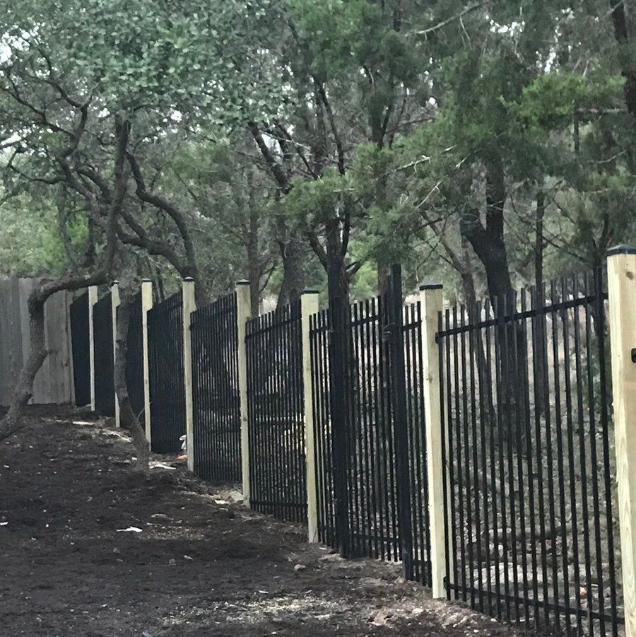 A black metal fence with wooden posts surrounded by trees
