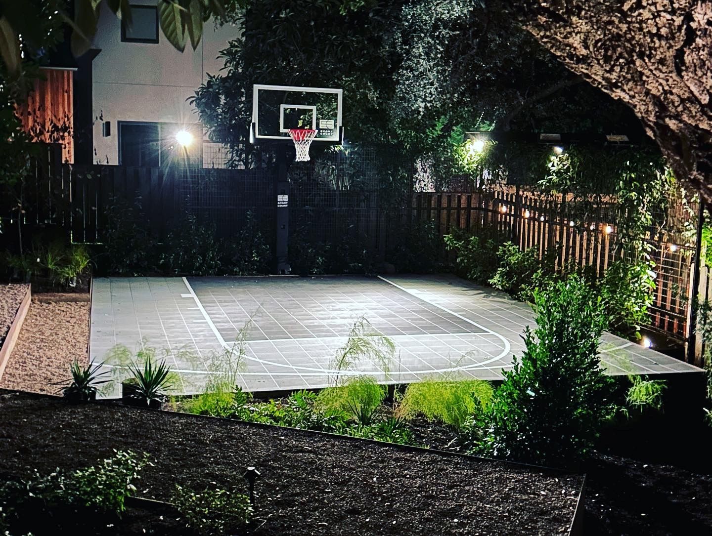 A backyard basketball court is lit up at night