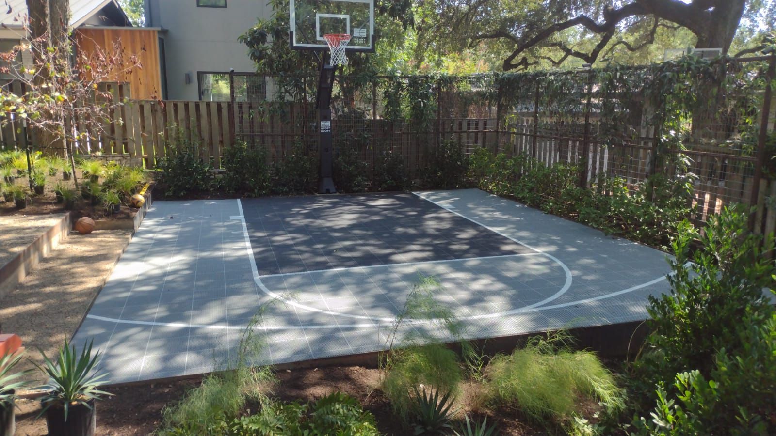A basketball court in the backyard of a house surrounded by trees.